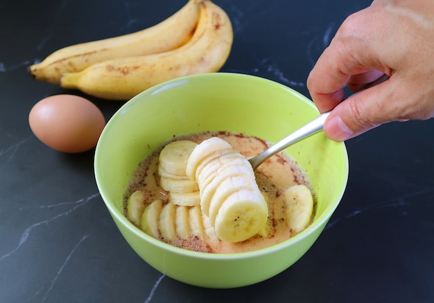 Tranches de banane mûre dans un bol à mélanger avec un autre ingrédient pour la cuisson du pouding au pain aux bananes