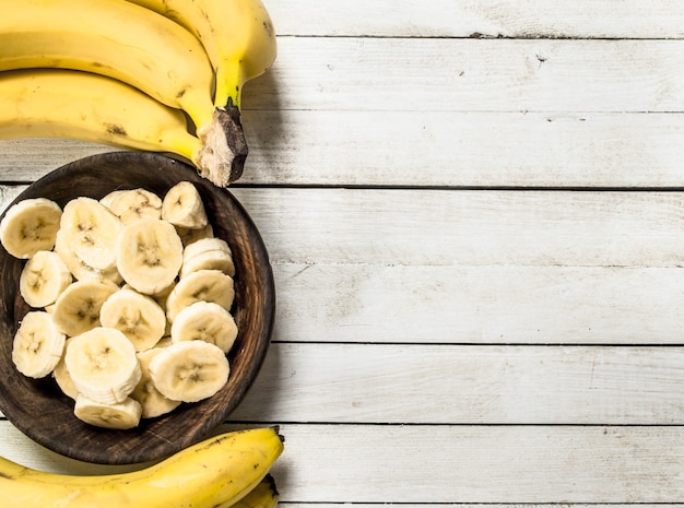 Tranches de bananes dans un bol en bois. Sur un fond en bois blanc.