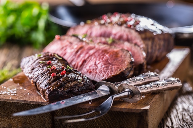 Tranches de bifteck de faux-filet moyen juteux sur planche de bois avec fourchette et couteau herbes épices et sel