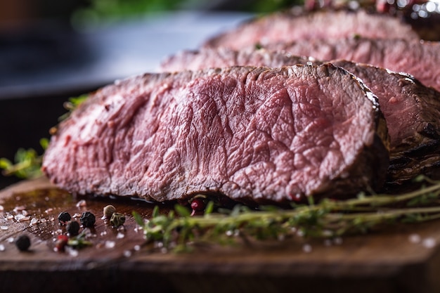 Tranches de bifteck de faux-filet moyen juteux sur planche de bois avec fourchette et couteau herbes épices et sel