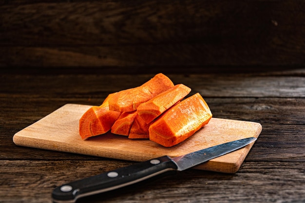 Tranches de carottes douces crues sur une planche à découper en bois avec un couteau.