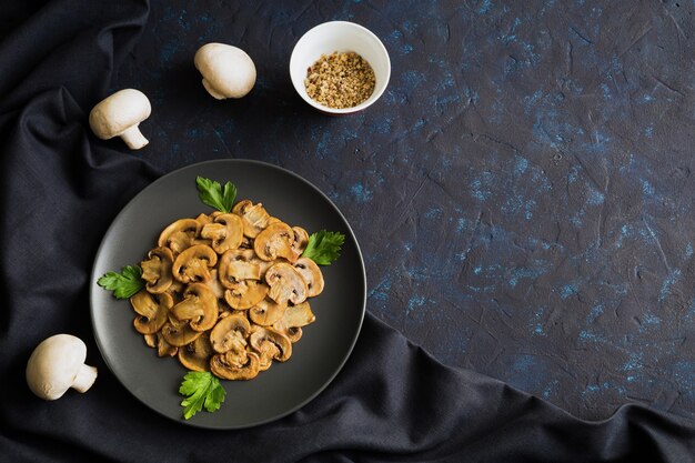 Tranches de champignons frits sur plaque noire décorée de champignons et de textiles à plat sur fond sombre avec espace copie