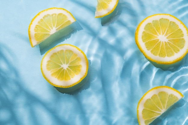 Des tranches de citron dans l'eau sur un fond bleu avec l'ombre et les vagues de près Le motif rafraîchissant d'été ou le concept de papier peint Vue supérieure et espace de copie