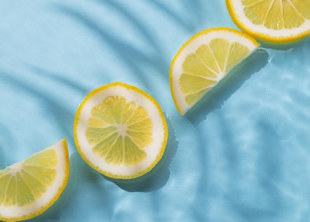 Des tranches de citron dans l'eau sur un fond bleu avec l'ombre et les vagues de près Le motif rafraîchissant d'été ou le concept de papier peint Vue supérieure et espace de copie