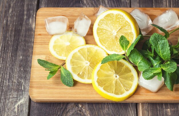 Tranches de citron, feuilles de menthe et glaçons sur une planche à découper