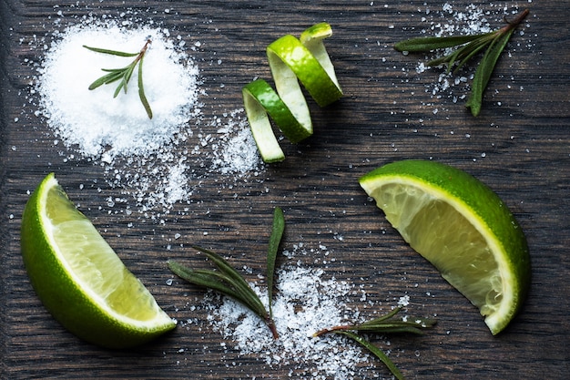 Tranches de citron vert frais, sel et romarin sur une planche à découper en bois.