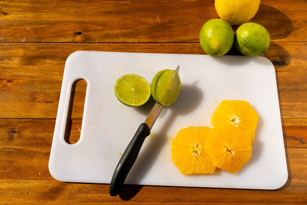 Tranches de citron vert et d'orange fraîchement coupées sur une planche à découper blanche avec un couteau