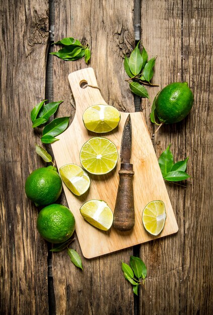 Tranches de citron vert sur une planche de bois avec des feuilles et un couteau.