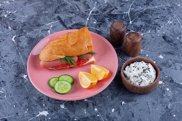 Tranches de citrons et de concombre, sandwich sur une assiette à côté d'un bol de fromage, sur le bleu.