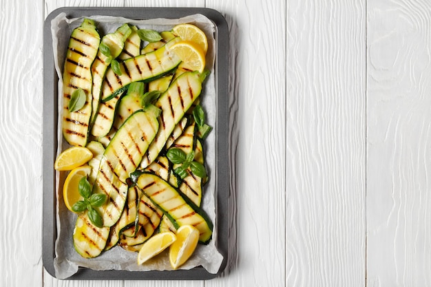 Tranches de courgettes grillées sur une plaque avec des feuilles de citron et de basilic frais, mise à plat, espace libre, cuisine italienne