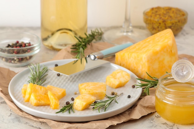 Tranches de délicieux fromage marbré avec un brin de romarin, du miel et un couteau à fromage et du vin blanc sur une assiette sur un fond de béton clair.