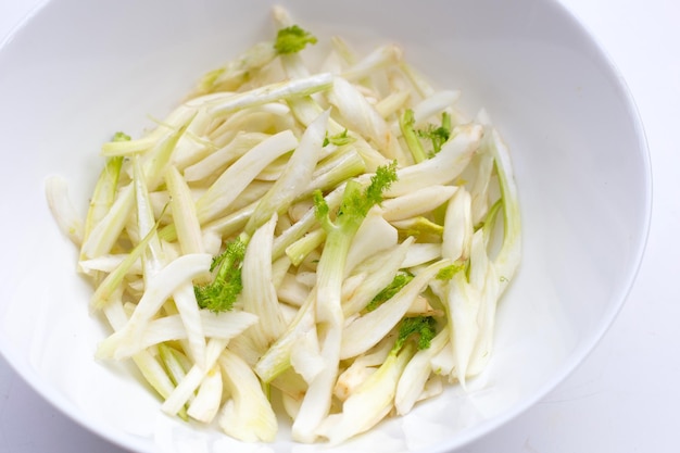 Tranches de fenouil frais dans un bol blanc sur fond blanc