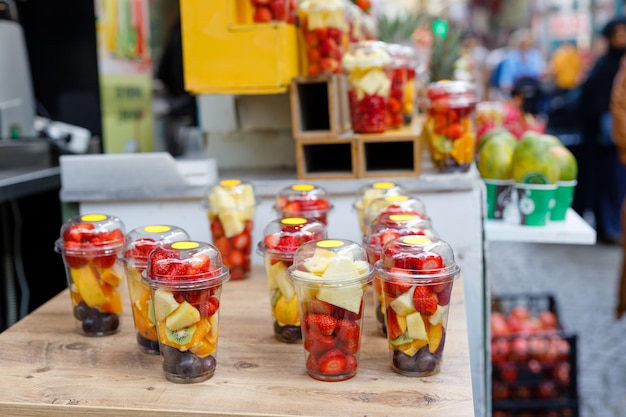 Tranches de fruits dans des gobelets en plastique transparent avec des fourchettes sur un comptoir de marché de rue Fruits lumineux rafraîchissants par une chaude journée ensoleillée d'été