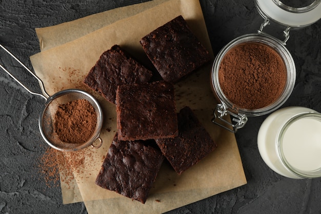 Tranches de gâteau au chocolat, bouteille de lait et passoire avec de la poudre sur fond noir, vue de dessus