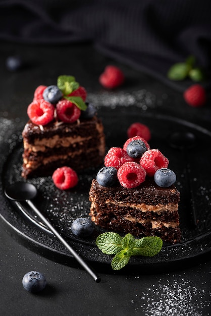 Tranches de gâteau au chocolat fait maison avec des fruits frais sur une plaque noire, vue du dessus