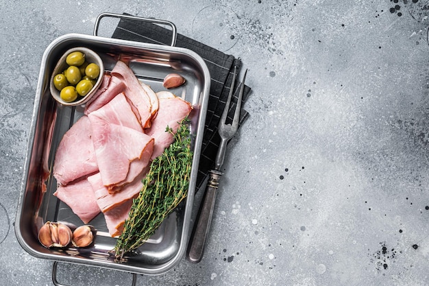 Tranches de jambon dans un bac de cuisine avec herbes et olives Prosciutto cotto italien Fond gris Vue de dessus Espace de copie