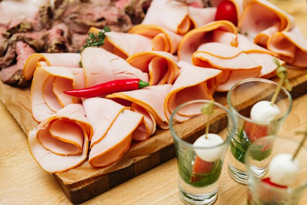 Photo des tranches de jambon fumé sur une planche de bois des tranches minces de charcuterie et de canapés caprese en coups closeup