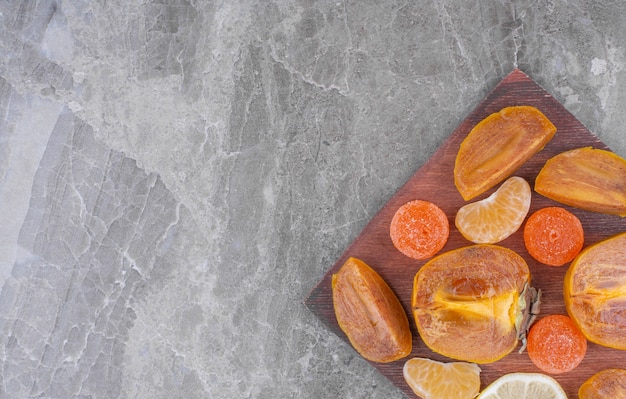 Tranches de kaki frais et de mandarines sur une planche à découper en bois.