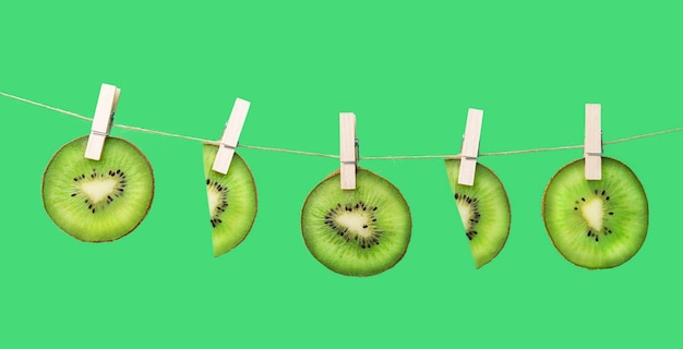 Tranches de kiwi accrochées à une ficelle avec des pinces Fruits tropicaux suspendus à une corde à linge sur fond vert