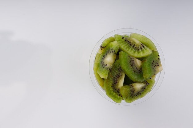 Tranches de kiwi ou morceau coupé disposés dans un verre transparent avec un fond de couleur blanche.