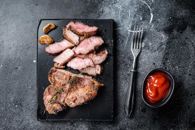 Tranches de longe de porc grillées sur planche de marbre Fond noir Vue de dessus