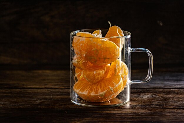 Tranches de mandarine pelées dans un verre sur un fond en bois.