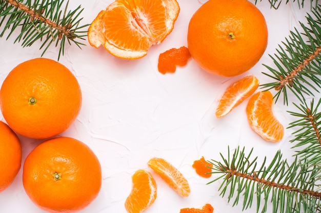 Tranches de mandarines purifiées, de mandarines entières et de branches de sapin sur une table blanche, vue de dessus