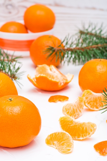 Tranches de mandarines purifiées, mandarines entières et branches de sapin sur une table blanche