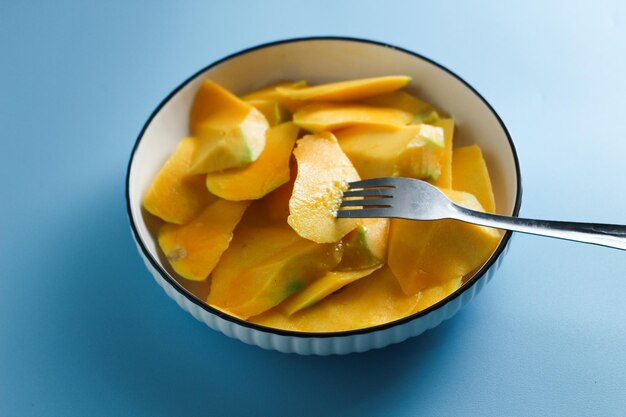 Photo tranches de mangue sur une assiette de salade blanche sur fond bleu clair