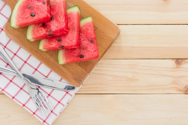 Tranches de melon d&#39;eau sur une planche de bois, servi avec des couverts et une serviette sur une table en bois