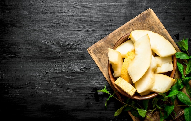 Tranches de melon mûr à la menthe fraîche. Sur la table en bois noire.