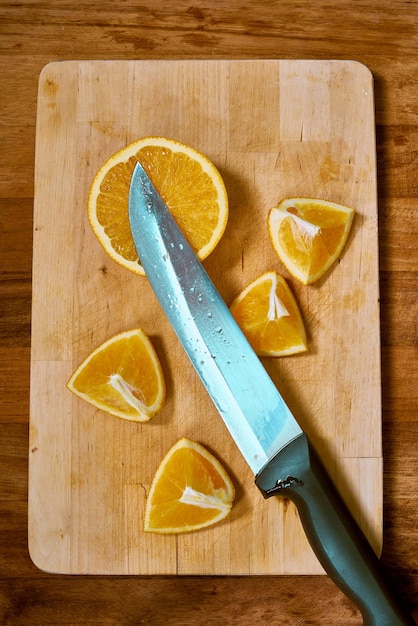 Tranches d'orange fraîche et un couteau à fruits sur une planche à découper en bois.