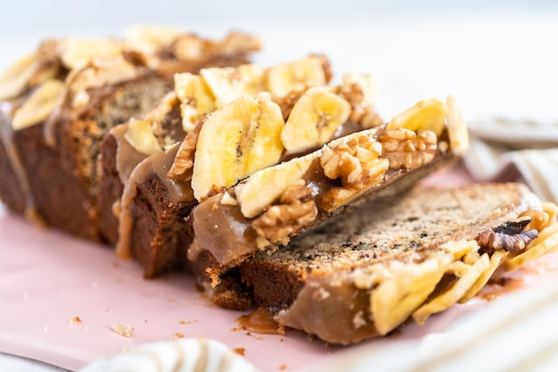 Tranches de pain aux bananes et noix arrosées de caramel maison sur une planche à découper rose.