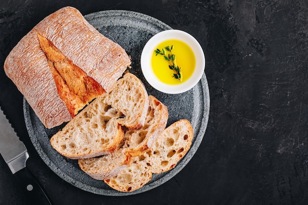 Tranches de pain ciabatta italien avec de l'huile d'olive sur une plaque de pierre sur fond de béton foncé vue de dessus copie espace