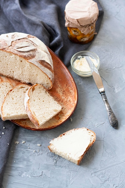 Tranches de pain maison avec beurre, couteau et pot sur fond gris