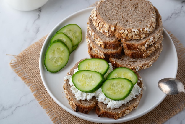 Tranches de pain de seigle avec fromage cottage et concombres sur fond blanc