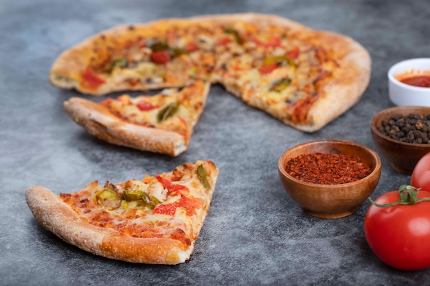 Tranches de pizza délicieuse chaude avec des tomates rouges fraîches placées sur une table en pierre.