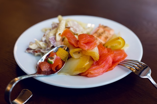 Tranches de poisson rouge sur une plaque blanche sur laquelle il y a une fourchette en acier courbé et une cuillère sur la table en bois marron