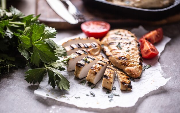 Tranches de poitrine de poulet grillées sur papier avec des herbes de céleri et des tomates.