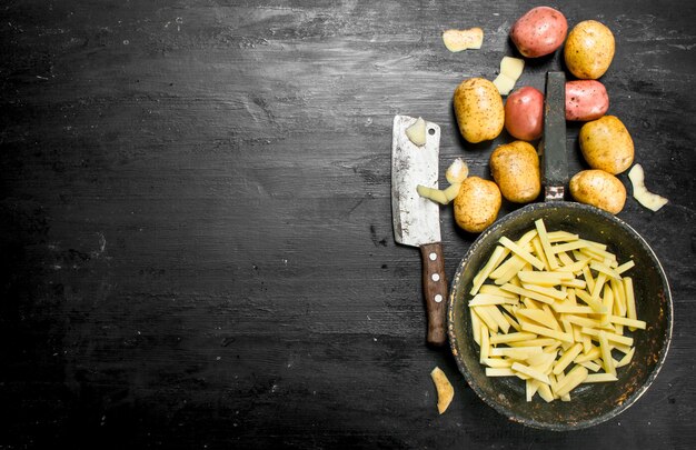 Tranches de pommes de terre dans une vieille poêle. Sur le tableau noir.