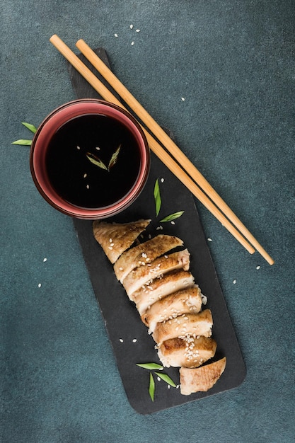 Tranches de poulet teriyaki sur un tableau noir graphite avec baguettes et sauce soja sur fond sombre. Nourriture asiatique. Orientation verticale. Vue de dessus avec un espace de copie pour le texte.