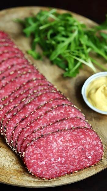 Tranches de salami au poivre noir sur une planche de bois Salami fumé cru