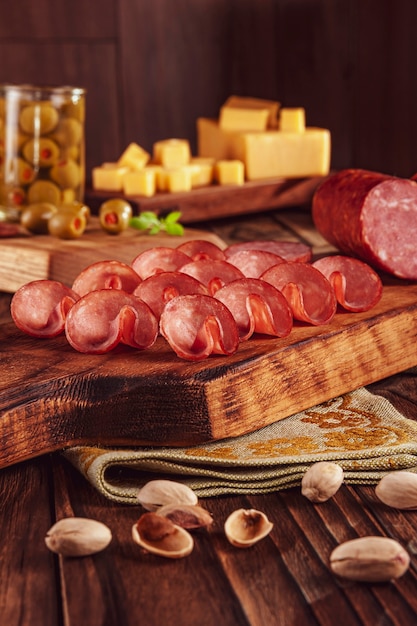 Tranches de salami fumé sur une planche à découper avec des cubes de fromage, olives, châtaignes et pistaches