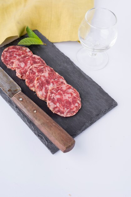 Tranches de saucisse sur ardoise, couteau, verre vide et drap jaune