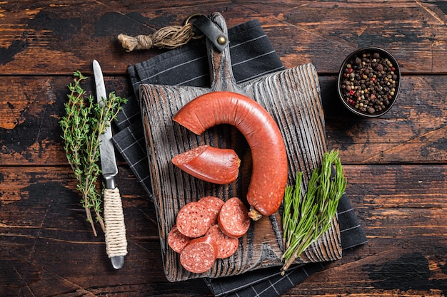 Tranches de saucisse de viande de boeuf Sucuk sur une planche à découper avec des herbes. Fond en bois. Vue de dessus.