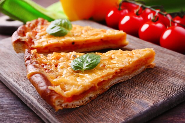 Tranches de savoureuse pizza au fromage avec basilic et légumes sur la table en gros plan