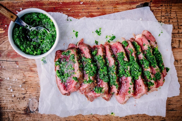 Tranches de steak de boeuf barbecue grillé avec sauce chimichurri verte sur fond de bois