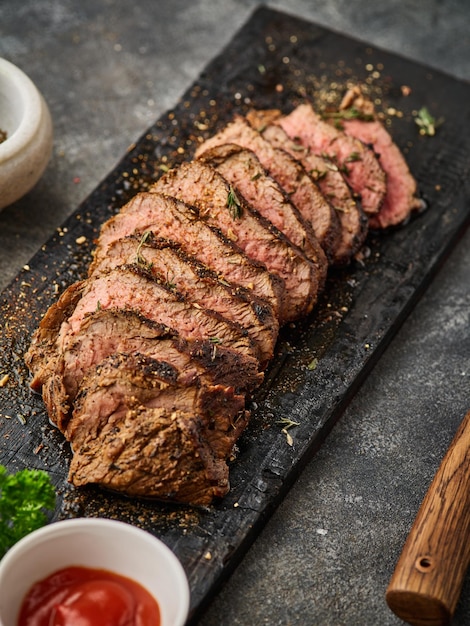 Tranches de steak de boeuf grillé sur une planche à découper au-dessus de la table grise Recette de filet mignon de steak de boeuf