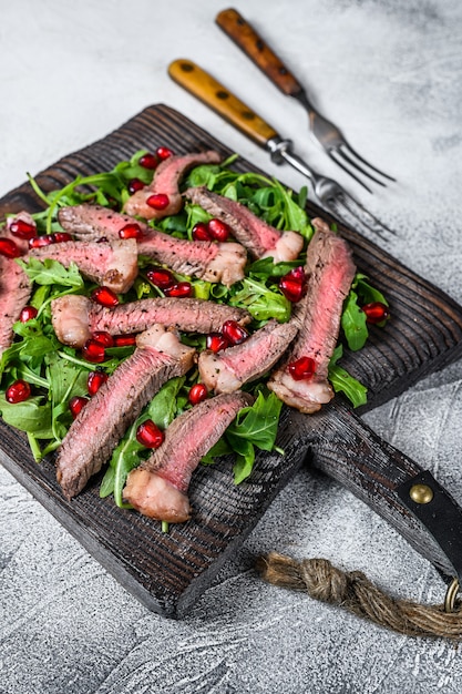 Tranches de steak de boeuf grillé avec salade de feuilles de roquette sur une planche à découper rustique.
