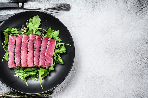 Tranches de steak de thon de poisson grillé dans une assiette avec salade de roquette.